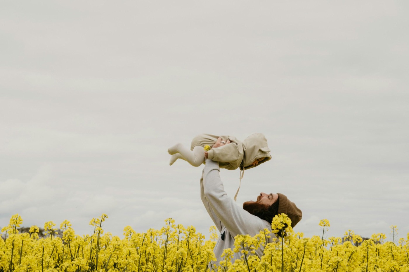 A parent lifting a baby into the air in a field of yellow flowers